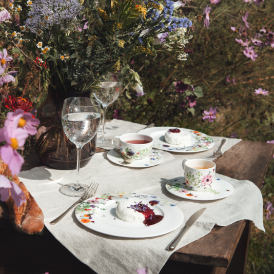 Wooden table set with floral Rosenthal tableware and tea in a blooming summer garden.